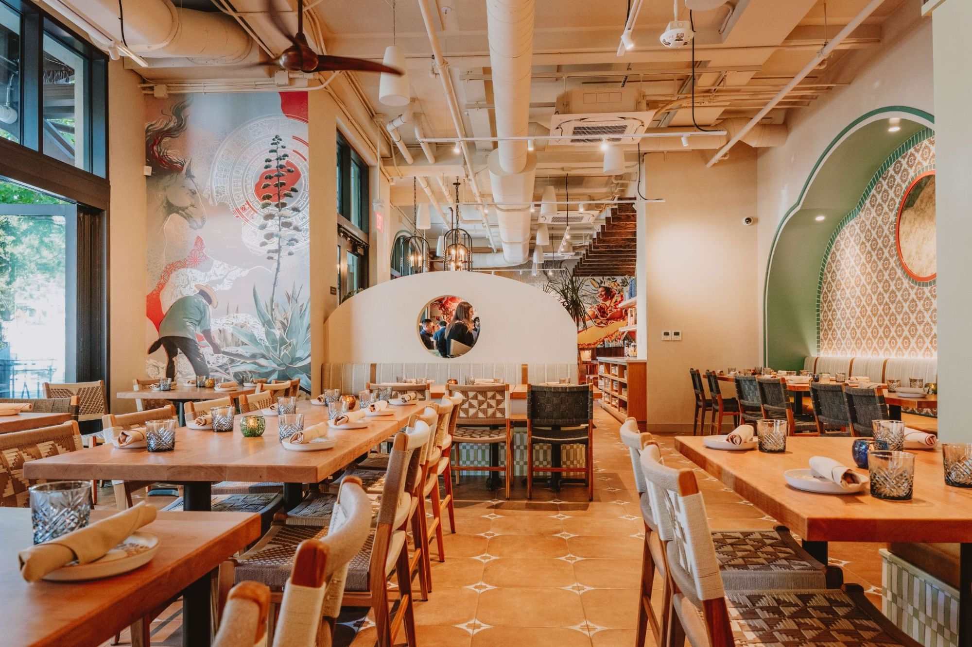 Alisios main dining room with long communal tables beneath an agave mural